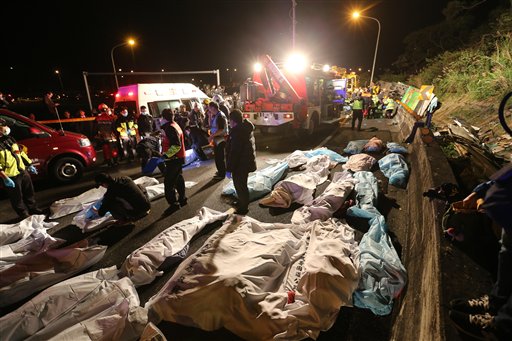 Varios cadáveres aparecen cubiertos en el lugar donde un autobús que llevaba turistas taiwaneses volcó el lunes 13 de febrero del 2017, en la salida de una autopista en la capital de Taiwán. El accidente dejó al menos 32 muertos y varios heridos, dijeron funcionarios. (AP Foto)